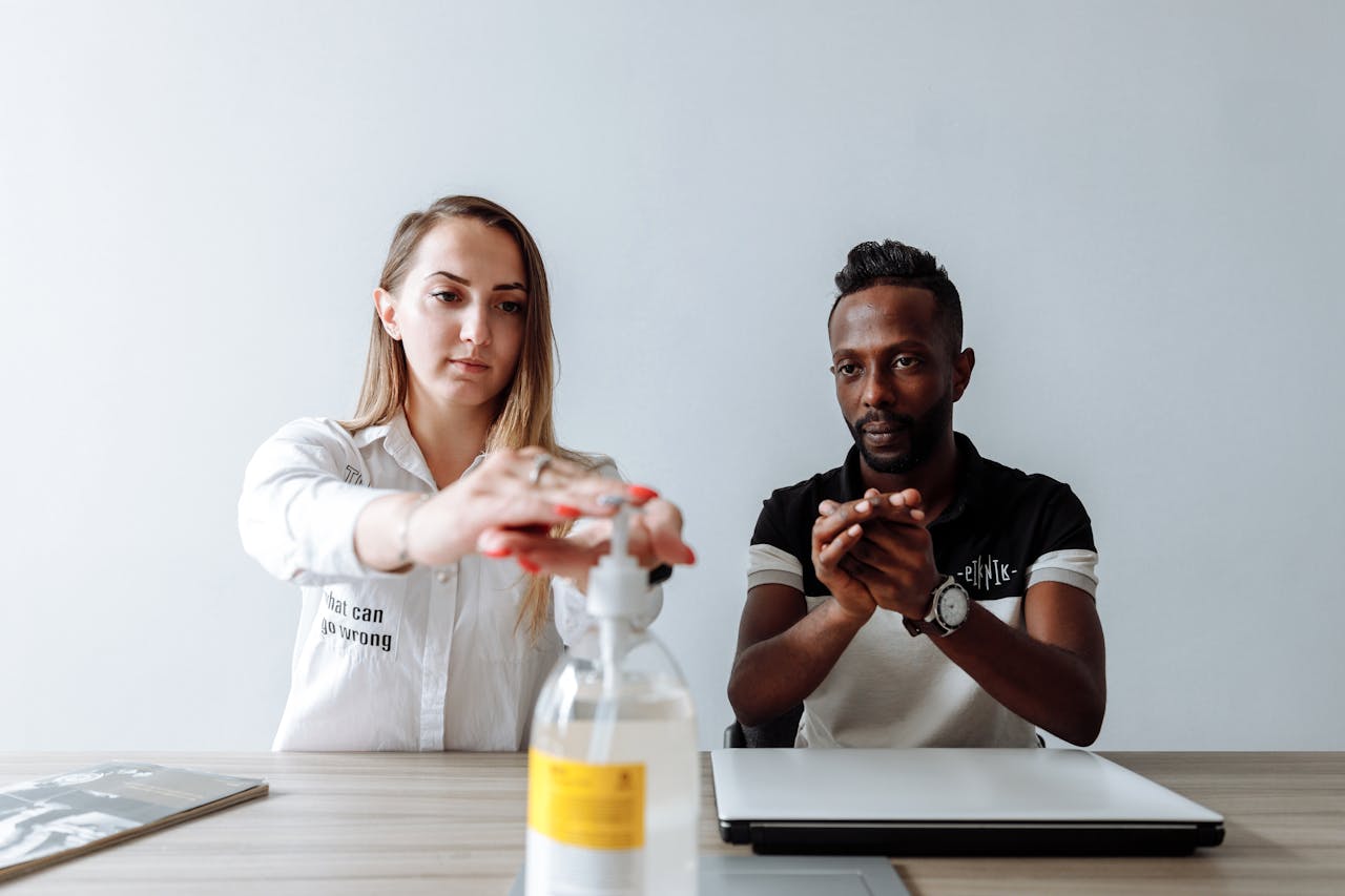 Two colleagues cleaning hands with sanitizer at a desk. Promotes hygiene.